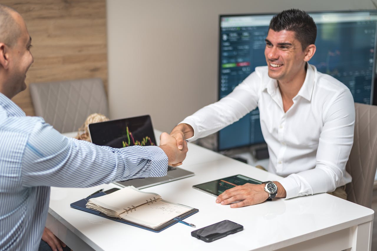 gallery-img-04 Two businessmen shaking hands in a modern office, indicating a successful deal or agreement.