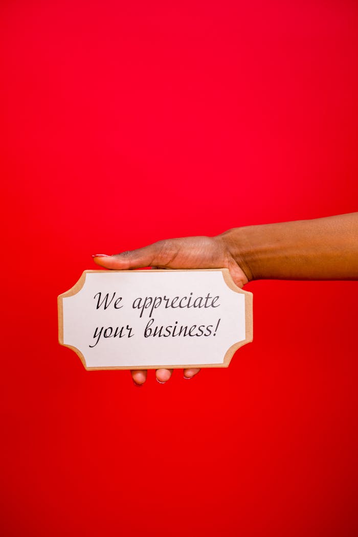 A hand holding an appreciation sign with the message 'We appreciate your business!' against a red backdrop.